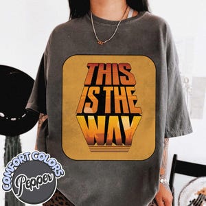 K&ouml;nnte beinhalten: Dunkelgraues T-Shirt mit dem Text "THIS IS THE WAY" in Orange und Gelb, vor braunem Hintergrund. Das Shirt hat ein Retro-Design und stammt aus der Comfort Colors Pepper Kollektion.