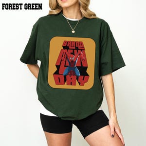 Puede incluir: Camiseta verde bosque con un gr&aacute;fico de Spider-Man y las palabras "BRAND NEW DAY". El dise&ntilde;o es rojo y amarillo sobre un fondo cuadrado. La camiseta tiene mangas cortas y el texto "FOREST GREEN" est&aacute; en la parte superior.