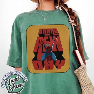 Puede incluir: Camiseta verde claro con un gr&aacute;fico retro de Spider-Man y las palabras "BRAND NEW DAY" en rojo y amarillo. La camiseta tiene una etiqueta Comfort Colors en un dise&ntilde;o circular.