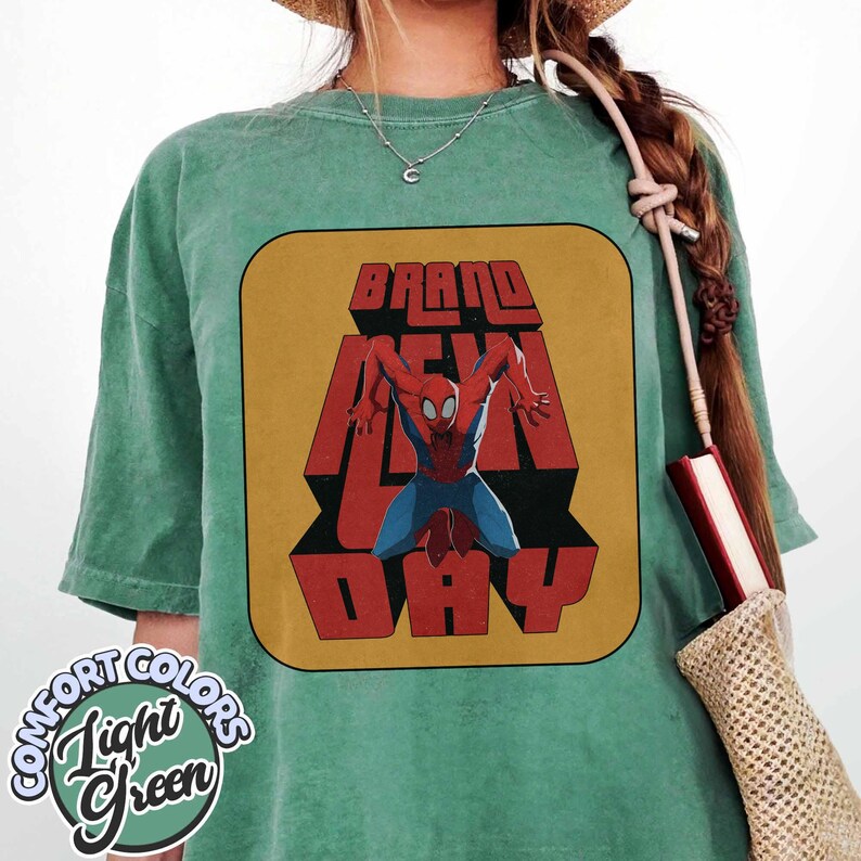 Puede incluir: Camiseta verde claro con un gr&aacute;fico retro de Spider-Man y las palabras "BRAND NEW DAY" en rojo y amarillo. La camiseta tiene una etiqueta Comfort Colors en un dise&ntilde;o circular.
