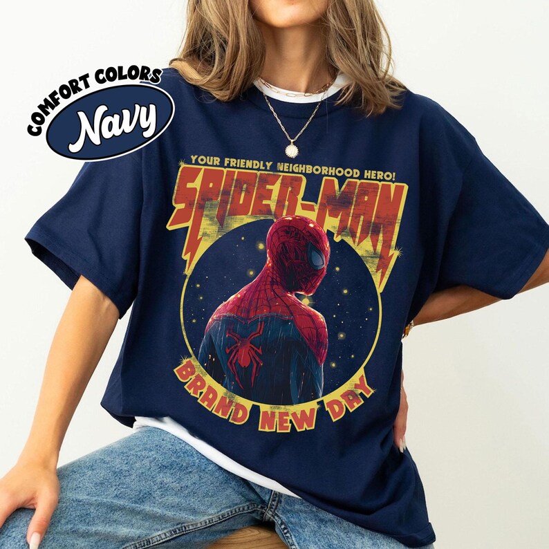 May include: Navy blue t-shirt featuring a graphic of Spider-Man with the text "Your Friendly Neighborhood Hero!" and "Brand New Day." The design includes a circular image of Spider-Man's back. The shirt has the words "Comfort Colors" and "Navy" in a circle.