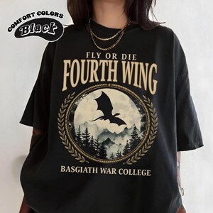 Puede incluir: Camiseta negra con el texto "FLY OR DIE FOURTH WING" y "BASGIATH WAR COLLEGE". El dise&ntilde;o presenta una silueta de drag&oacute;n en un marco circular con una escena de monta&ntilde;a y bosque. La camiseta tambi&eacute;n tiene el texto "COMFORT COLORS Black".