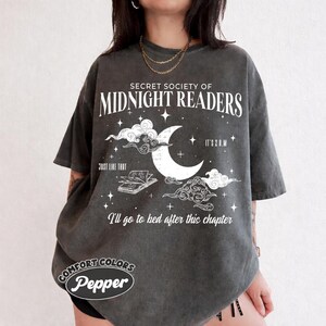 May include: A charcoal gray short-sleeve t-shirt featuring white graphic text that reads Secret Society of Midnight Readers, It's 2 A.M., Just Like That, and I'll go to bed after this chapter, with a crescent moon, stars, and an open book.