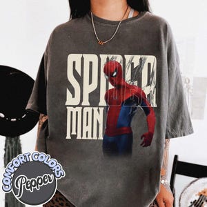 Peut inclure: T-shirt gris fonc&eacute; avec un graphisme de Spider-Man en costume rouge et bleu, et l'inscription "SPIDER MAN" en blanc. Le t-shirt a un aspect vieilli et le nom de la marque "Comfort Colors Pepper" est visible.