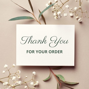 Puede incluir: Una tarjeta blanca con las palabras "Thank You FOR YOUR ORDER" en elegante escritura verde. La tarjeta est&aacute; rodeada de ramitas de flores blancas y hojas verdes, sobre un fondo neutro.