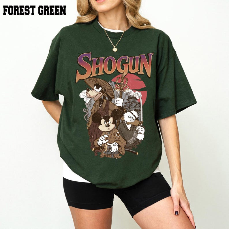 Puede incluir: Una camiseta verde bosque con un estampado gr&aacute;fico que incluye el texto SHOGUN en una fuente degradada. La ilustraci&oacute;n muestra a tres personajes de dibujos animados vestidos con atuendos japoneses tradicionales, incluyendo un sombrero c&oacute;nico y espadas.