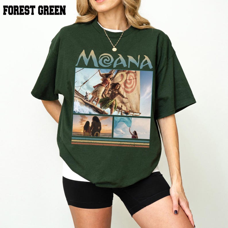 May include: A forest green short-sleeve t-shirt featuring a graphic print with the text MOANA. The design includes three panels showing scenes from the movie Moana, including characters on a boat, a sunset silhouette, and a person holding blue fabric.