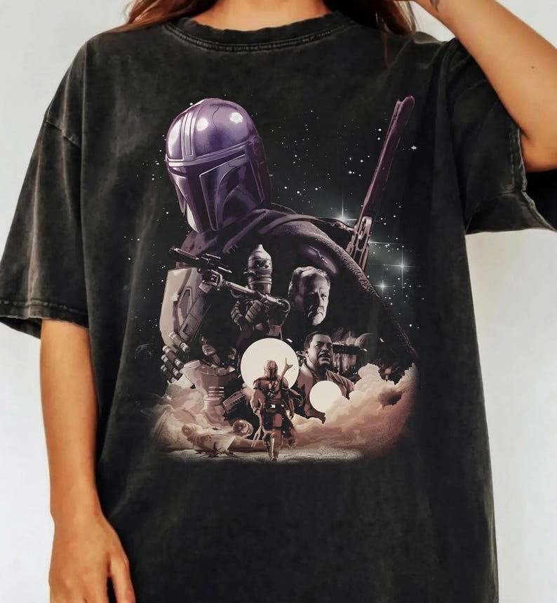 K&ouml;nnte beinhalten: Dunkelgraues T-Shirt mit einem Motiv aus einer Science-Fiction-Serie. Das Design zeigt eine Figur mit Helm, andere Charaktere und eine Sternenszene. Das T-Shirt hat einen Vintage-Look.