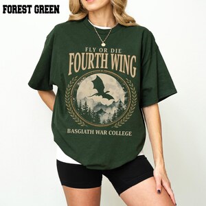 Puede incluir: Camiseta verde bosque con el texto "FLY OR DIE FOURTH WING" y un gr&aacute;fico de un drag&oacute;n frente a un paisaje monta&ntilde;oso. La camiseta tambi&eacute;n tiene el texto "BASGIATH WAR COLLEGE".