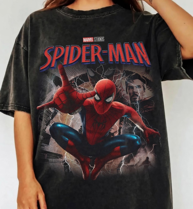 May include: A charcoal grey short-sleeve t-shirt featuring a graphic print of Spider-Man in a dynamic pose with web-shooting hands. The design includes the text Marvel Studios and Spider-Man in red and blue, alongside an image of Doctor Strange.