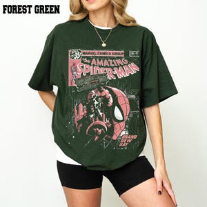 Peut inclure: T-shirt vert for&ecirc;t avec un design de couverture de bande dessin&eacute;e de The Amazing Spider-Man. Le graphisme comprend le personnage de Spider-Man, du texte de bande dessin&eacute;e et le logo Marvel Comics Group. Le t-shirt a des manches courtes et un col rond.