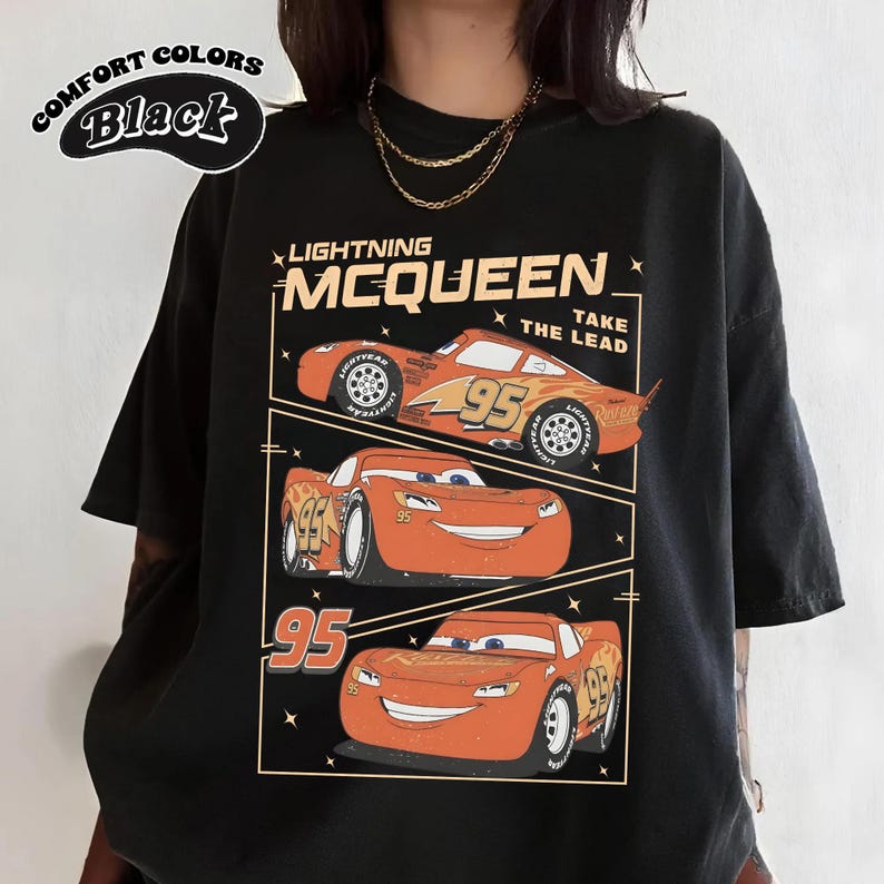 May include: Black t-shirt featuring Lightning McQueen from the Cars movie. The design includes three images of the character with the number 95 and the text "Lightning McQueen Take The Lead". The shirt also has the text "Comfort Colors Black".