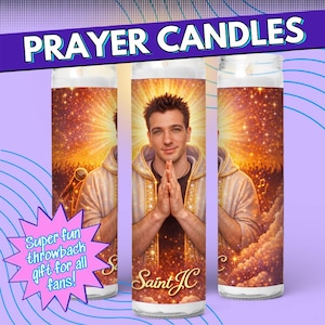 Op de afbeelding: Drie gebedkaarsen met een portret van een man met gevouwen handen. De kaarsen hebben een gouden en bruine achtergrond met de tekst "PRAYER CANDLES" bovenaan en "Saint JC" onderaan. Een roze ster zegt "Super fun throwback gift for all fans!"