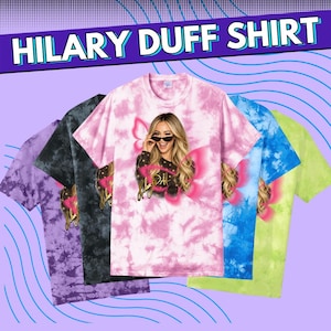 Puede incluir: Camisetas teñidas con tinte anudado en morado, negro, rosa, azul y verde. Cada camiseta presenta un gráfico de una mujer con gafas de sol y alas de mariposa, con el texto "HILARY DUFF SHIRT" en la parte superior.