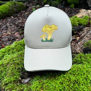 Peut inclure: Une casquette de baseball beige avec un motif de champignon jaune. Le champignon est représenté avec un petit champignon poussant sur le plus grand.