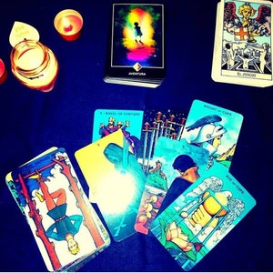 May include: A tarot card reading spread with ten cards laid out on a dark blue surface. The cards include "The Hanged Man", "Wheel of Fortune", "Knight of Cups", "Ace of Cups", and "El Juicio".