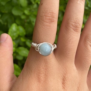 May include: A silver wire wrapped ring with a light blue gemstone.
