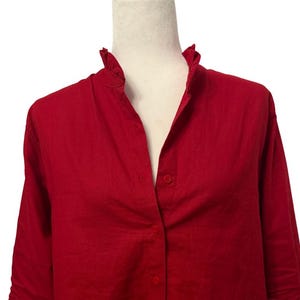 K&ouml;nnte beinhalten: Ein leuchtend rotes Hemd mit R&uuml;schenkragen und langen &Auml;rmeln, die an den Ellbogen hochgekrempelt sind. Das Hemd wird mit Kn&ouml;pfen vorne geschlossen und ist aus leichtem Material.