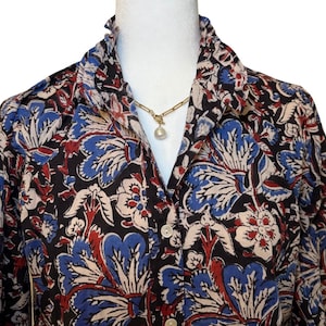 May include: A black, blue, and red floral print long-sleeve shirt with a ruffled collar and a pearl necklace.