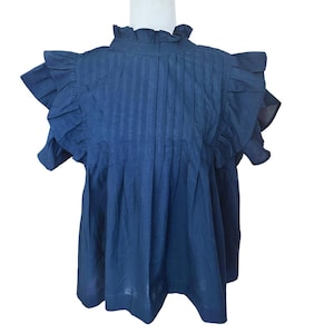 Puede incluir: Una blusa azul oscuro de manga corta con cuello y mangas con volantes. La blusa tiene un frente plisado y un ajuste holgado.