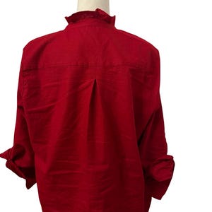 K&ouml;nnte beinhalten: Ein leuchtend rotes Langarmhemd mit R&uuml;schenkragen und gekn&ouml;pften Manschetten. Die R&uuml;ckseite des Hemdes hat eine Falten-Detail. Das Hemd wird auf einer wei&szlig;en Schaufensterpuppe pr&auml;sentiert.