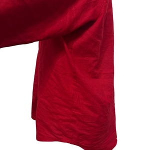 K&ouml;nnte beinhalten: Nahaufnahme eines leuchtend roten Kleidungsst&uuml;cks, m&ouml;glicherweise ein Hemd oder Kleid, mit flie&szlig;endem, strukturiertem Stoff. Das Material drapiert sich weich und deutet auf ein leichtes Textil hin. Die leuchtende Farbe dominiert den Rahmen vor wei&szlig;em Hintergrund.
