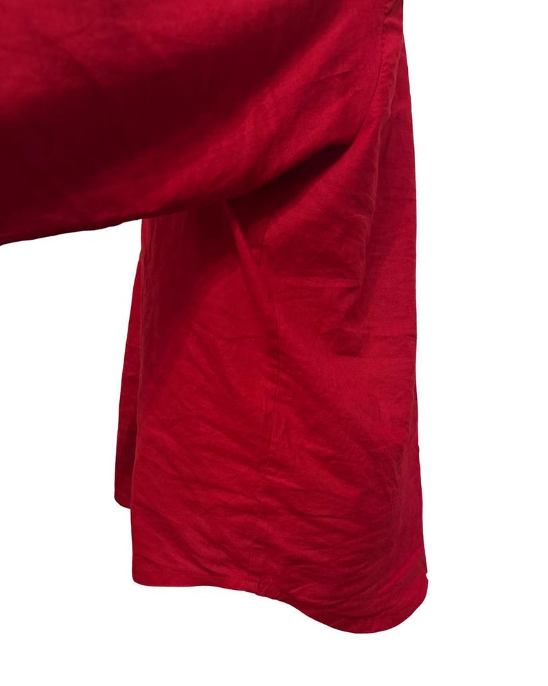 K&ouml;nnte beinhalten: Nahaufnahme eines leuchtend roten Kleidungsst&uuml;cks, m&ouml;glicherweise ein Hemd oder Kleid, mit flie&szlig;endem, strukturiertem Stoff. Das Material drapiert sich weich und deutet auf ein leichtes Textil hin. Die leuchtende Farbe dominiert den Rahmen vor wei&szlig;em Hintergrund.