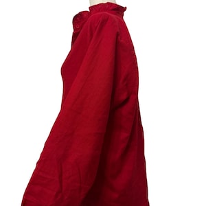 K&ouml;nnte beinhalten: Ein rotes Langarmhemd mit R&uuml;schenkragen und Knopfverschluss. Das Hemd wird auf einem wei&szlig;en Mannequinkopf pr&auml;sentiert, der das Seitenprofil und die &Auml;rmeldetails zeigt. Der Stoff scheint eine subtile Textur zu haben.