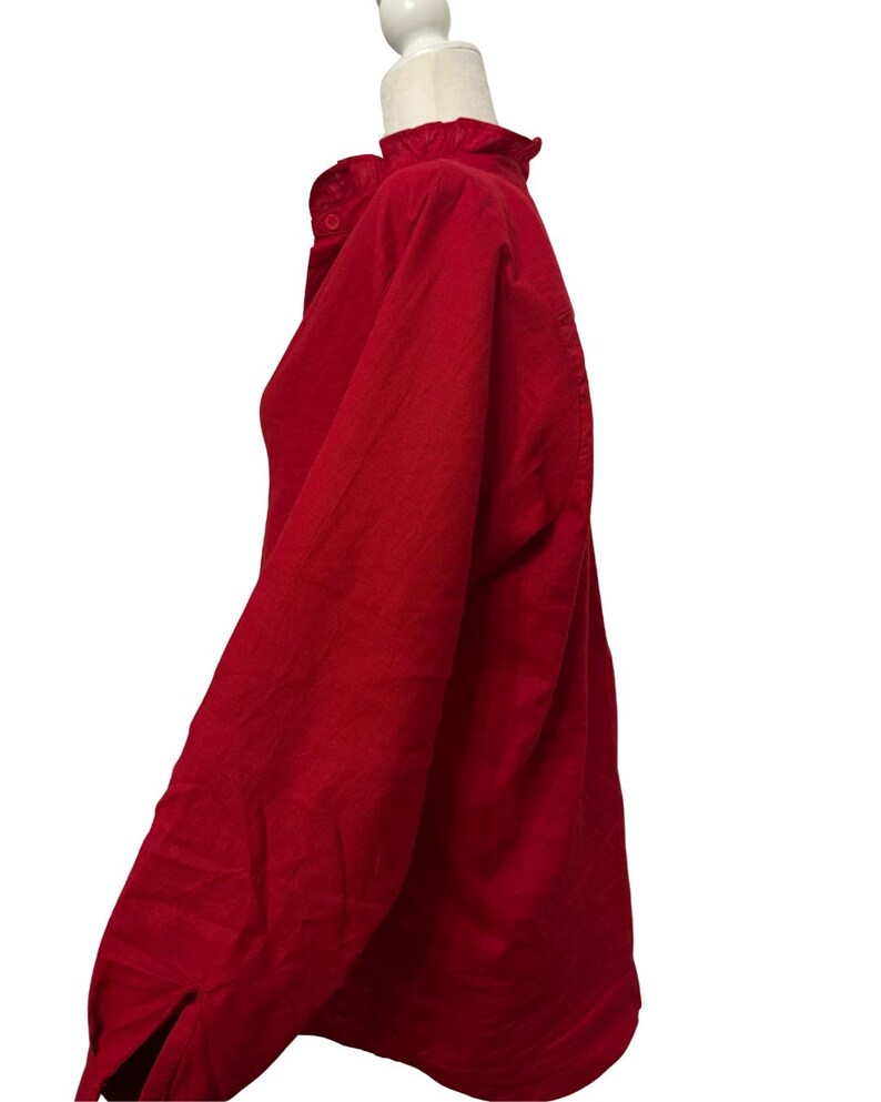 K&ouml;nnte beinhalten: Ein rotes Langarmhemd mit R&uuml;schenkragen und Knopfverschluss. Das Hemd wird auf einem wei&szlig;en Mannequinkopf pr&auml;sentiert, der das Seitenprofil und die &Auml;rmeldetails zeigt. Der Stoff scheint eine subtile Textur zu haben.