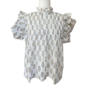 Puede incluir: Blusa blanca de algodón con cuello de volantes y mangas cortas. La blusa tiene un estampado paisley en color marrón claro.