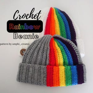 May include: Two crocheted beanies, one gray with a rainbow stripe and one white with a rainbow stripe. The text "Crochet Rainbow Beanie" is written on the image. The text "pattern by umphi_creates" is written below the beanies.