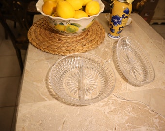 May include: Two clear glass serving dishes with a diamond pattern. The dishes are oval and round, and are sitting on a light brown marble surface.
