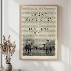 May include: A framed print featuring the text "LARRY MCMURTRY LONESOME DOVE" in a bold font. The background is a collage of text, with a sepia-toned image of horses in a field. The print has a wooden frame.