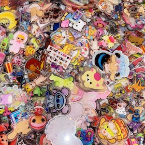 May include: A large collection of colorful acrylic charms featuring various cartoon characters, animals, and shapes. The charms are layered together, displaying diverse designs including bears, rabbits, and fantasy figures with glossy finishes.