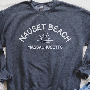 May include: A dark gray sweatshirt with white text that reads "Nauset Beach Massachusetts" and a graphic of a sun rising over the ocean.