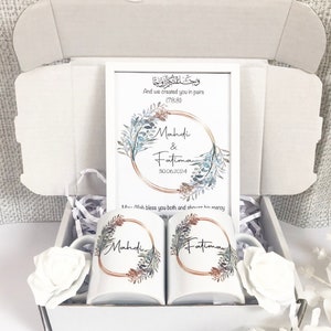 Könnte beinhalten: Eine weiße Geschenkbox mit einem weißen Rahmen im Inneren. Der Rahmen hat ein Aquarell-Blumenmuster mit den Namen Mahdi & Fatima und dem Datum 30.06.2024. Die Box enthält außerdem zwei weiße Tassen mit dem gleichen Blumenmuster und den Namen Mahdi und Fatima. Der Text im Rahmen lautet: "Und wir haben euch in Paaren erschaffen (78.8)" und "Möge Allah euch beide segnen und seine Barmherzigkeit schenken".