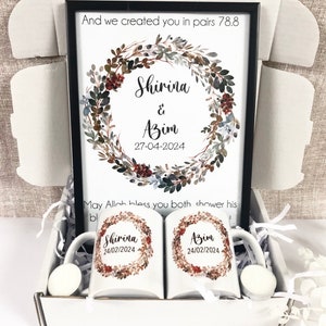Könnte beinhalten: Ein Geschenkset mit einem gerahmten Druck, der einen Aquarellkranz mit den Namen Shirina & Azim und dem Datum 27-04-2024 zeigt. Der Text "And we created you in pairs 78.8" befindet sich oben auf dem Druck. Die Box enthält außerdem zwei weiße Tassen mit den Namen Shirina und Azim und dem Datum 24/02/2024, die darauf gedruckt sind.