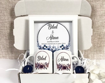 May include: A gift box containing two white mugs, a framed print, and two candles. The mugs are decorated with floral designs and the names "Bilal" and "Alina". The framed print displays the names "Bilal & Alina" and the date "2nd March 2024".