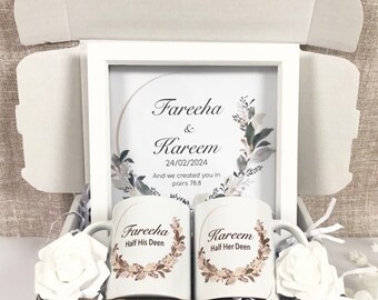 May include: A white gift box containing a framed print and two mugs. The print reads "Fareeha & Kareem 24/02/2024" with floral accents. The mugs say "Fareeha Half His Deen" and "Kareem Half Her Deen". White roses are also in the box.