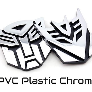 May include: Two chrome-finished PVC plastic emblems, featuring a stylized geometric design. The emblems have a shiny, reflective surface and are set against a white background. The text "PVC Plastic Chrome" is displayed below the emblems.