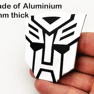 May include: A silver and black emblem made of aluminum, 2mm thick. The emblem features a geometric design with a white background and black accents. The text "Made of Aluminium" is visible at the top.