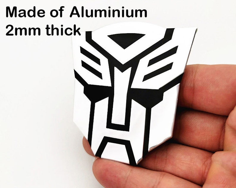 May include: A silver and black emblem made of aluminum, 2mm thick. The emblem features a geometric design with a white background and black accents. The text "Made of Aluminium" is visible at the top.