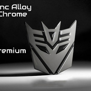 May include: A chrome-finished emblem with a geometric design, featuring the text "Zinc Alloy Chrome" and "Premium". The emblem has a metallic sheen and is set against a dark background.