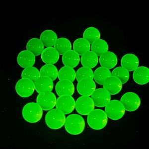 May include: A cluster of luminous green glass marbles on a black backdrop. The spherical marbles emit a bright, even glow, creating a striking visual effect. These marbles are a playful and engaging item.