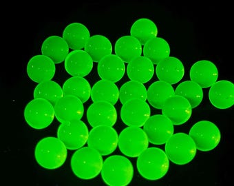May include: A cluster of luminous green glass marbles on a black backdrop. The spherical marbles emit a bright, even glow, creating a striking visual effect. These marbles are a playful and engaging item.