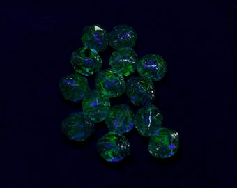 May include: A collection of faceted, round beads. The beads are a translucent green with blue and green internal colour variations. The beads are scattered on a dark blue background, creating a sparkling effect.