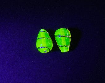 May include: Two neon green, teardrop-shaped glass beads. Each bead is wrapped with thin, silver-coloured wire. The beads are set against a dark blue background.