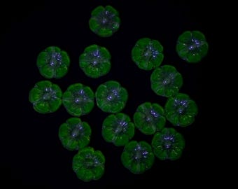 May include: A collection of fifteen small, translucent green glass beads shaped like five-petaled flowers. Each bead features a central hole and a rounded, moulded petal design with a glossy finish, arranged in a scattered pattern against a black background.