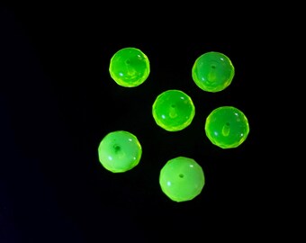 May include: Six luminous green beads on a black backdrop. The beads are spherical with a central hole, and seem to be made of a translucent material. The beads are scattered across the image.