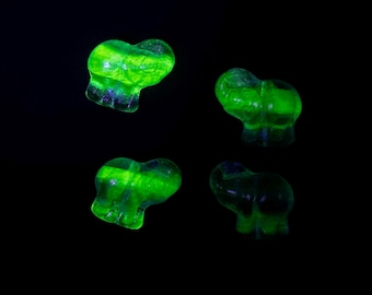 May include: Four small, translucent elephant-shaped figurines that glow with a vibrant neon green light against a solid black background. Each figurine displays a smooth, rounded form with subtle carved details representing the head, trunk, and body.